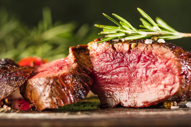 Nahaufnahme eines in Scheiben geschnittenen medium-rare Steaks mit einem Zweig frischem Rosmarin auf der Oberseite, das eine angebratene äußere Schicht und ein rosafarbenes, saftiges Inneres zeigt - perfekt für jede Grill-Catering- oder BBQ-Catering-Veranstaltung.