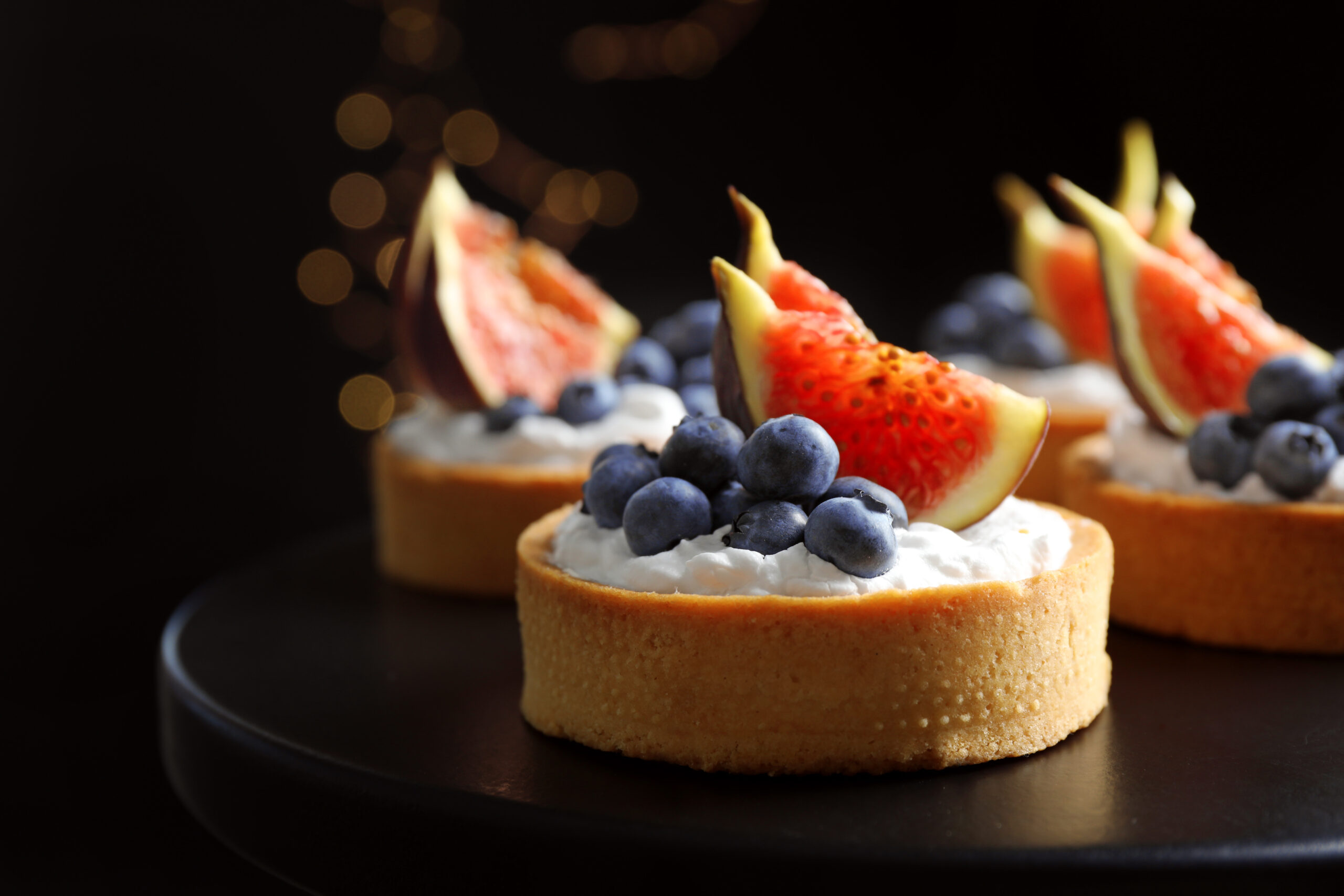 tarts with blueberries and figs on black table against dark back