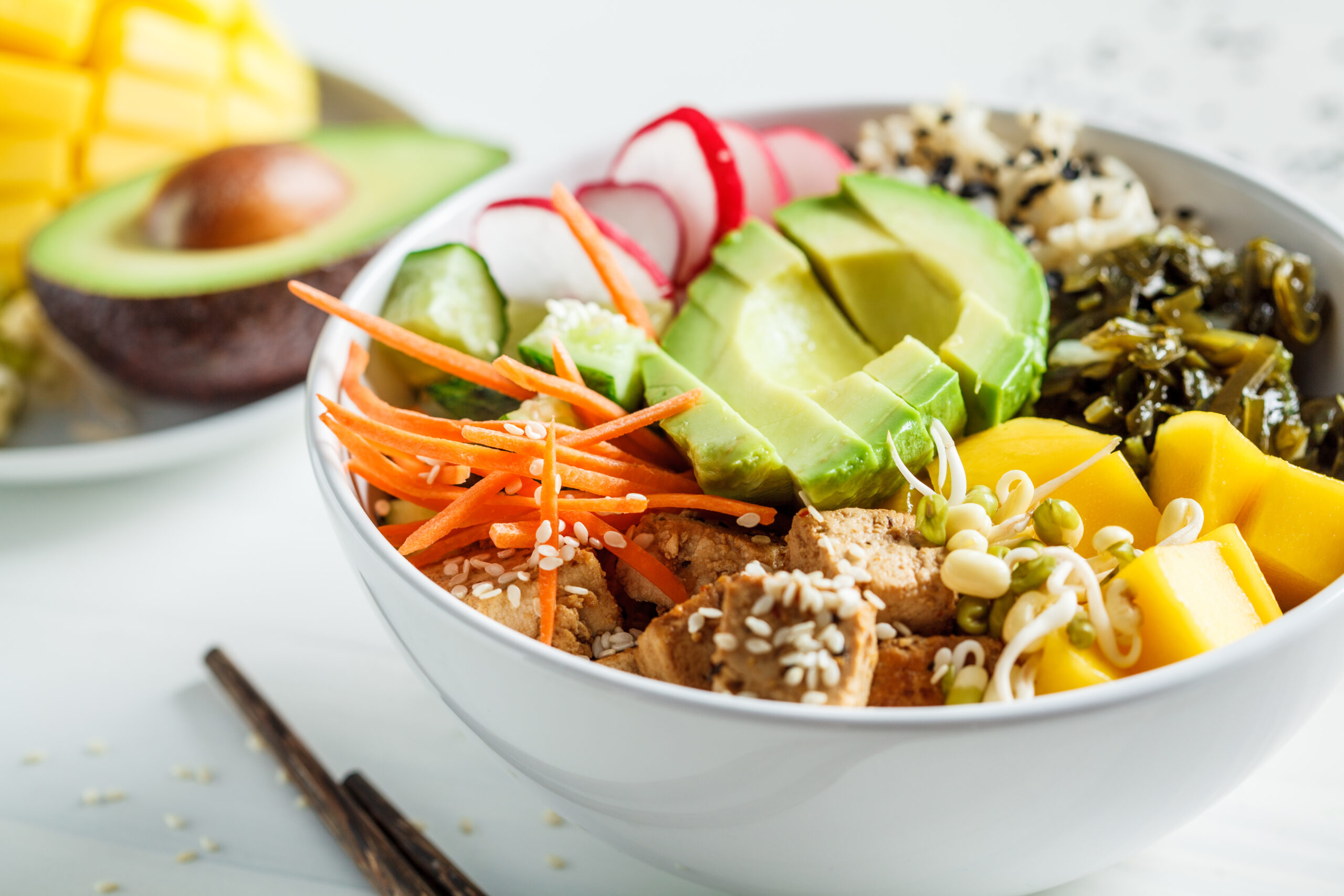 vegan poke bowl with avocado, tofu, rice, seaweed, carrots and mango. vegan food concept.